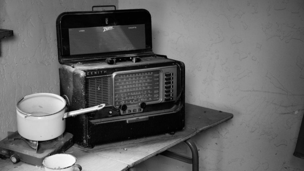 grayscale photo of vintage radio beside stove with cooking pot